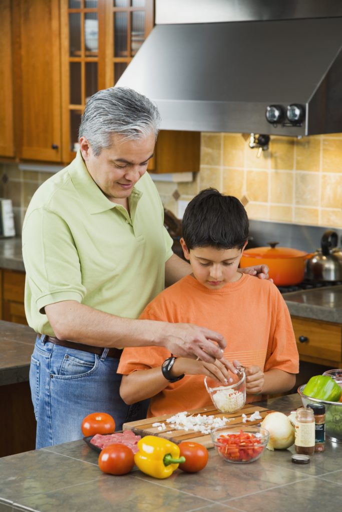A man helps a boy measure cooking ingredients.