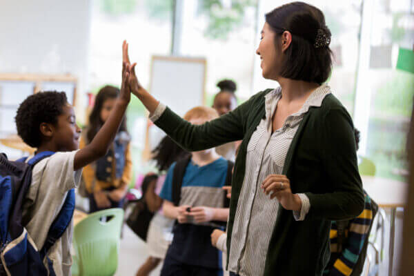 Cheerful young Hispanic elementary school teacher gives a high five to a student before class.