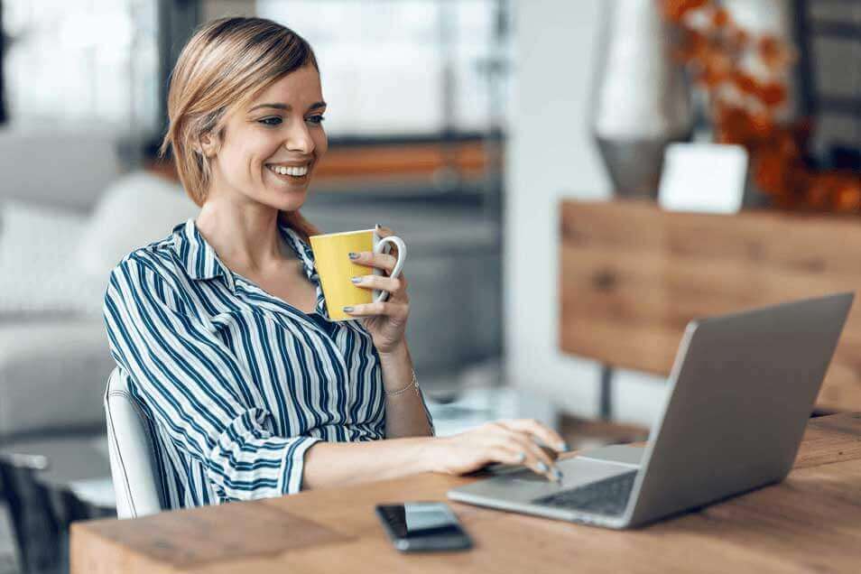 Shot of smiling young business woman working with computer while drinking coffee in the living room at home.